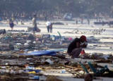 A Thai man surrounded by the damage caused by a tsunami squats on the sand at Patong beach in Phuket, December 27, 2004. One of the most powerful earthquakes in history hit Asia on Sunday, unleashing a tidal wave which devastated coastal areas of Sri Lanka, India, Indonesia and tourist isles in Thailand, killing tens of thousands of people. REUTERS/Luis Enrique Ascui